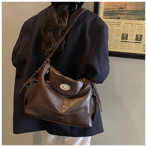 Detail of dark brown leather tote bag showing metallic twist lock and broad shoulder strap