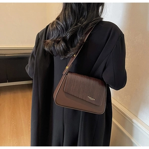 Detail of dark brown shoulder bag with woven texture lid and wide leather strap