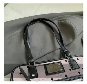 Detail of pink polka dot handbag with black leather handles and silver metallic logo