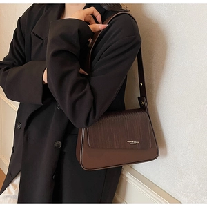 Detail of dark brown leather crossbody bag with textured flap and gold embossed text