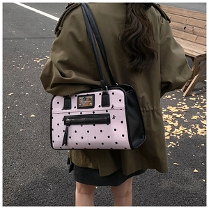 Detail of pink polka dot canvas backpack featuring a black bow and golden logo plate