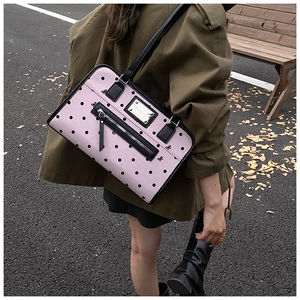 Detailed view of pink polka dot handbag with black leather trim and functional zipper pocket
