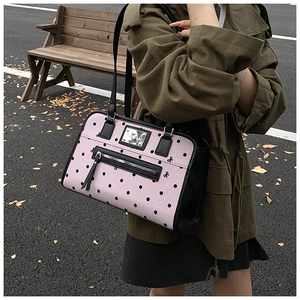 Pink tote bag with black polka dots shown on a wooden bench in an outdoor street setting