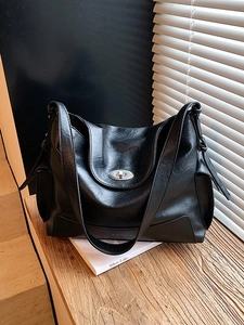 Black leather tote bag with silver oval twist lock on a wooden desk with window light