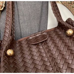 Close-up of woven brown leather tote bag with gold studs and colorful jacquard strap