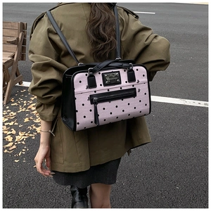 Close-up of pink polka dot backpack featuring black leather trim and metal logo plate