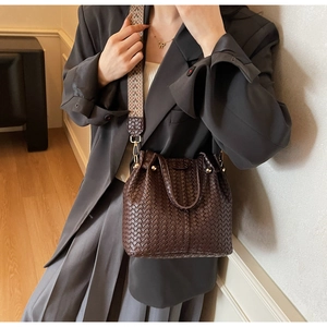 Detail of dark brown woven bucket bag featuring a wide geometric ethnic strap on shoulder