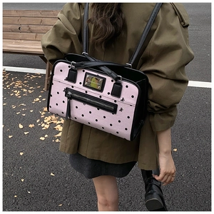 Pink polka dot backpack detail showing black bow accents and metal brand plaque outdoors