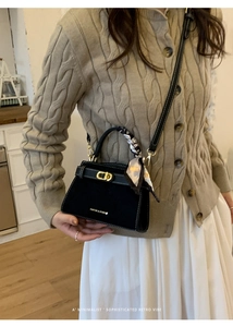 Detalle del bolso Kelly negro mate con cierre dorado y asa envuelta en pañuelo