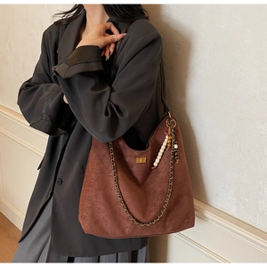 Détail du sac bandoulière en daim marron foncé avec boucle dorée et pendentif perlé