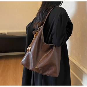 Detail view of large dark brown leather tote with tassel charm worn by model