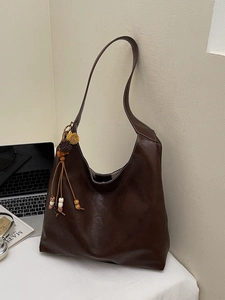 Brown large capacity leather tote bag with ethnic tassel pendant on white desk