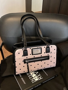 Pink polka dot tote bag with black bows and leather handles on a stylish chair