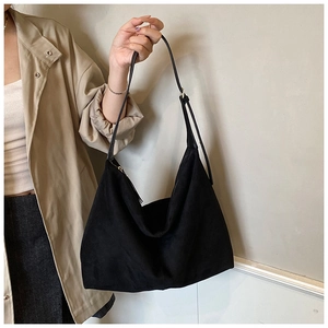 Detail view of a black suede hobo shoulder bag with an adjustable strap on a trench coat