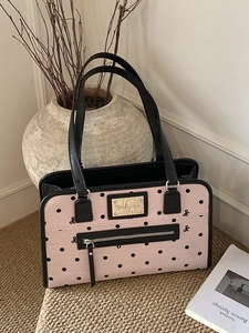 Vintage pink polka dot tote bag with black leather straps and golden metal logo plaque