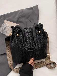 Retro black woven bucket bag with patterned wide strap on a grey blazer background