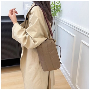 Gros plan sur un sac bandoulière en nylon matelassé marron porté avec un manteau kaki