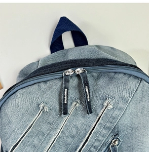 Detail of gradient denim backpack showing top handles, dual zippers, and distressed texture