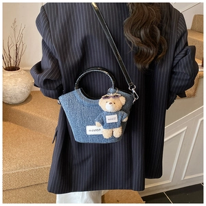 Détail du sac seau en denim avec breloque ours en peluche porté à l'épaule par le modèle