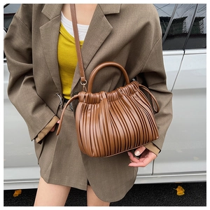 Detail of a brown pleated PU leather bucket bag with top handle and adjustable strap