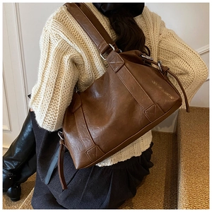 Close-up of brown textured leather shoulder bag with decorative stitching on wide strap