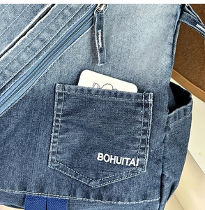 Detail of gradient blue denim backpack showing embroidered logo and front pocket
