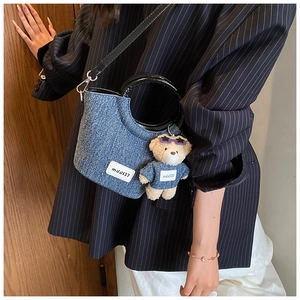 Detail of blue denim crossbody bag with black handles and a cute bear bag charm accessory