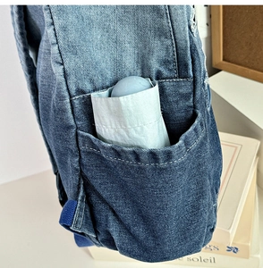 Detailed close-up of side pocket on blue denim backpack holding a folding umbrella