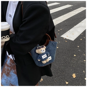 Détail du sac seau en denim bleu foncé avec poignée en cuir et breloque ourson