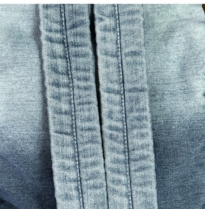 Macro shot of double-needle stitching and gradient blue wash texture on denim backpack