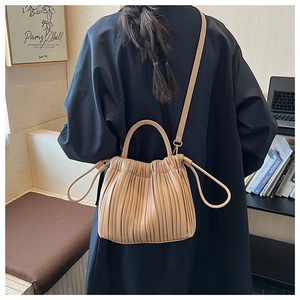 Dettaglio della borsa a secchiello beige plissettata con manico fisso e tracolla sottile urbana