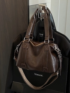 Deep brown PU leather Boston bag with wide woven strap hung on a classic black suit