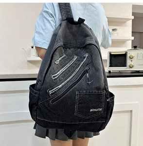 Detail view of washed denim backpack with triple diagonal zippers and frayed edge texture