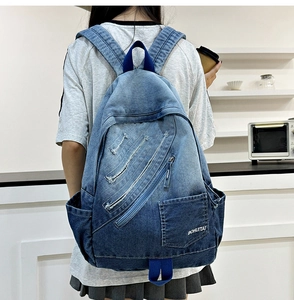 Detail of blue denim backpack showing multi-zipper pockets and vintage washed texture