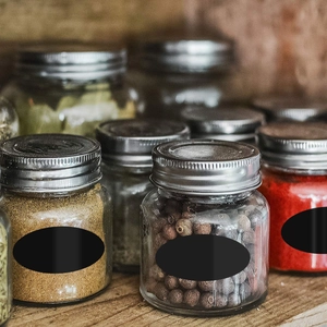 Close-up of glass spice jars with silver lids and black labels on a wooden shelf