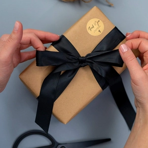 Hände verpacken Geschenkbox mit schwarzem Band und rundem Danke-Aufkleber aus Kraftpapier