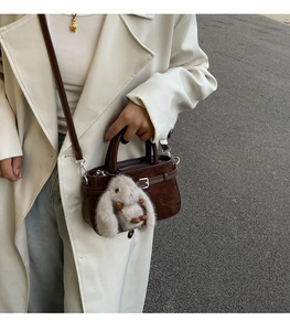 Détail du sac à main en daim marron foncé avec breloque lapin en peluche sur un mannequin