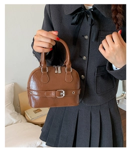 Close-up of vintage brown shell bag featuring glossy leather texture and metal buckles