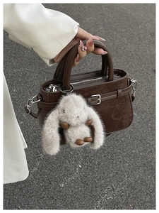 Détail du sac à main en daim marron foncé avec boucle décorative et breloque lapin