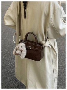 Détail du sac à main en cuir marron foncé avec boucle décorative et breloque lapin