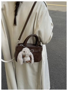 Détail d'un sac à main marron en daim avec boucle décorative et breloque lapin en peluche