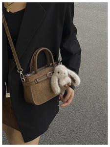 Sac à main vintage en daim marron avec porte-clés lapin porté sur un blazer noir