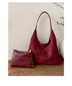 Détail d'un ensemble de sacs bordeaux en daim avec pochette zippée sur un bureau en bois