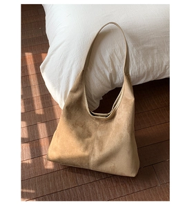 Détail du sac hobo en daim avec couture centrale sur parquet bois sous une lumière douce
