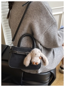 Détail d'un sac bandoulière noir avec charm lapin en peluche et finition texturée chic