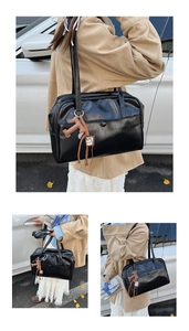 Detailed view of black glossy Boston bag featuring a stylish brown T-shaped leather charm