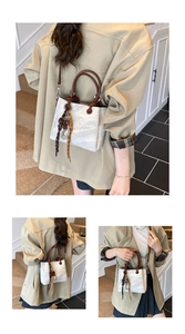 Detail of round dark handle and silk scarf charm on marble texture bucket bag