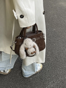 Sac bandoulière en cuir marron avec charme lapin porté avec un manteau en ivoire
