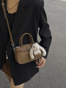 Sac bandoulière en daim marron avec poignées et charm lapin sur fond de rue urbaine
