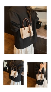 Detail of beige bucket bag with brown leather handles and a decorative bow charm